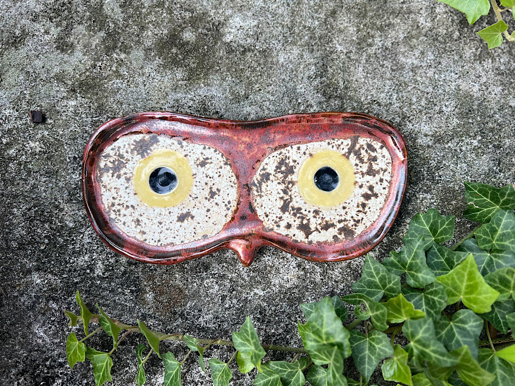 Ceramic eyeglass holder with owl design on a concrete surface with greenery