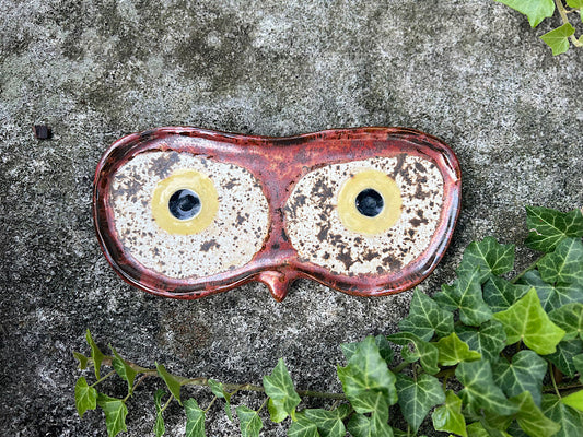 Ceramic eyeglass holder with owl design on a concrete surface with greenery